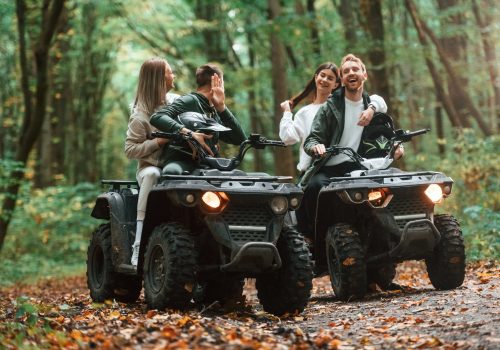 Smiling and having fun. Two couples on a quad bike in the forest during the day.