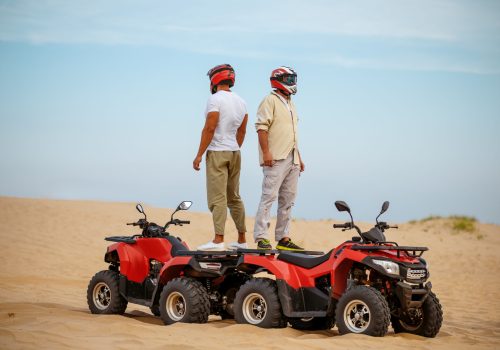 Two racers in helmets stand back to back on atvs, freedom riding in desert. Male persons on quad bikes, sandy race, dune safari in hot sunny day, 4x4 extreme adventure, quad-biking